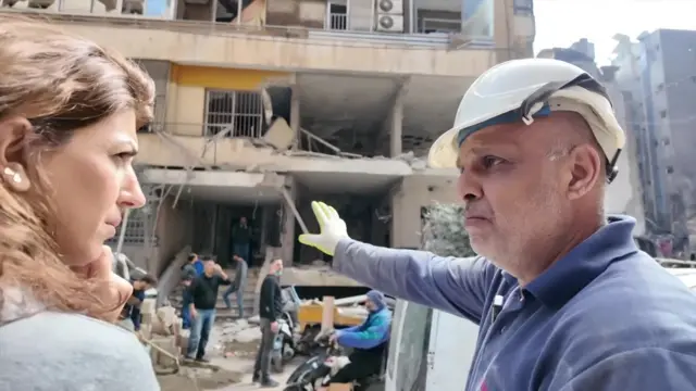 घायथ इटानी ने सफेद हेलमेट पहन रखा था और बीबीसी संवाददाता कैरिन टोर्बी से बात करते हुए उन्होंने अपना हाथ एक नष्ट हुई इमारत की ओर बढ़ाया।