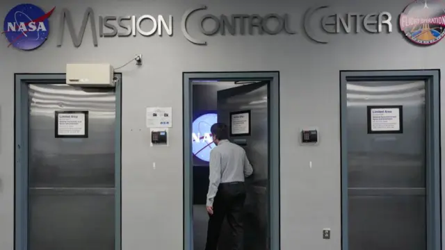 A man walks through the middle of three silver doors at Nasa's Mission Control Center