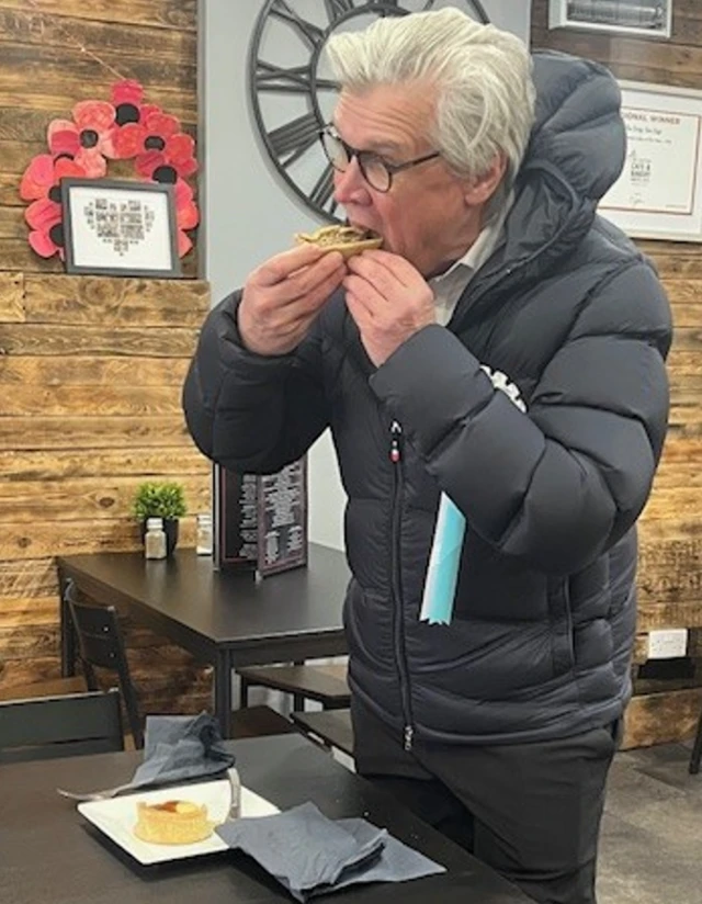 Malcolm Offord eats a Scotch pie while standing at a cafe table