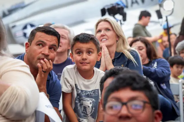A man and a child nervously look on amid a crowd gathered to watch the Artemis II mission return