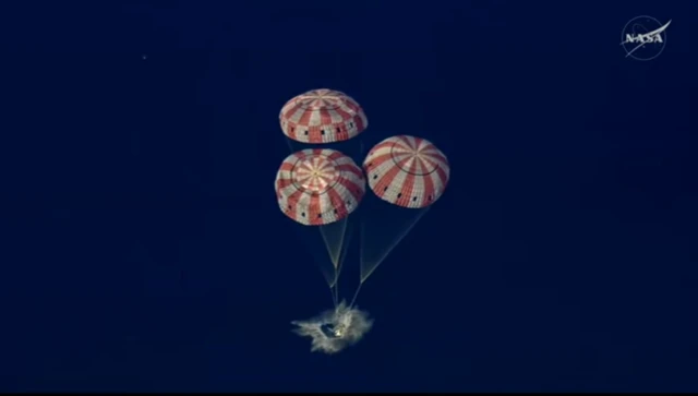Orion crew splashdown in Pacific Ocean, with the three main parachutes visible above