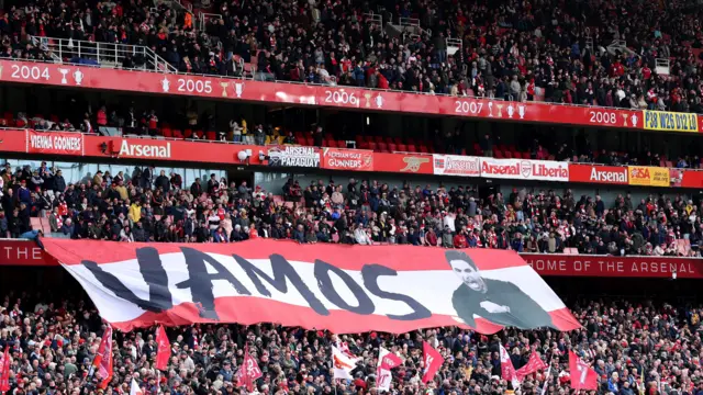 Fans hold up a banner that reads 'Vamos' intribute to Arteta