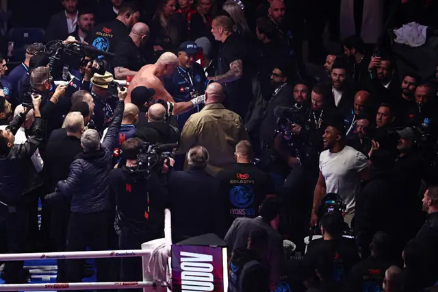 Tyson Fury leans over the ropes and points at a smiling Anthony Joshua