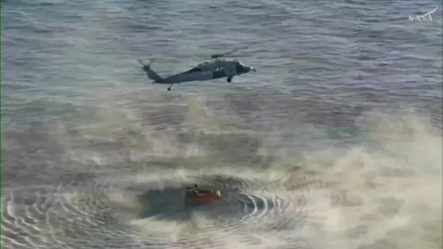 A helicopter above the Orion crew of the Artemis II mission, ready to extract them