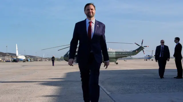 US Vice-President JD Vance walking on an airport tarmac with a helicopter and a jet plane in the background