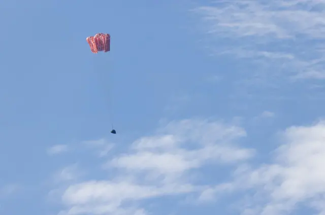 Nasa’s Orion spacecraft seen with its main parachutes deployed against a blue sky.