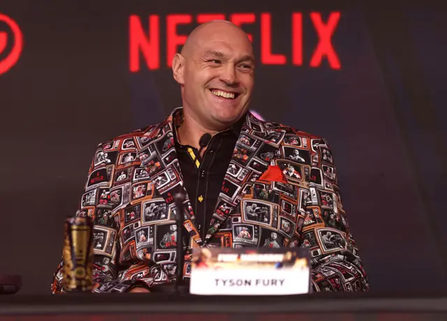 Tyson Fury sits at a table and smiles