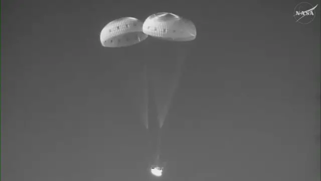 Orion with the three main parachutes deployed in a thermal imagine picture. The module is in bright white against a dark backdrop
