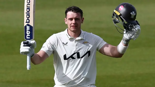 Jamie Smith raises his bat and helmet after scoring a century for Surrey against Leicestershire