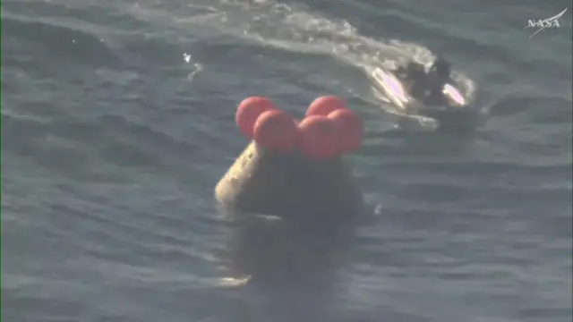 The Orion module in the Pacific Ocean with a small raft approaching it.