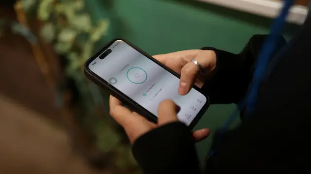 Close up photo of a pair of hands, one with a thumb ring, holding an iPhone with a nearly all-white screen to illustrate the internet blackout in Iran