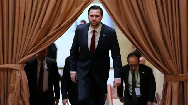 JD Vance walks through brown parted curtains with three officials behind him.