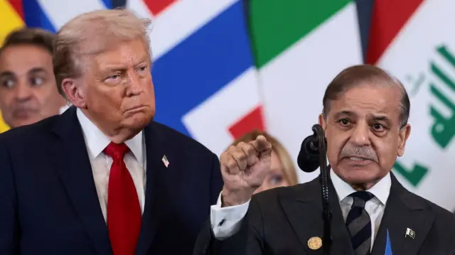 Donald Trump standing behind Pakistani Prime Minister Shehbaz Sharif as he speaks on a podium
