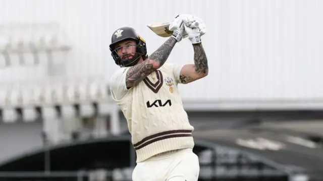 Jordan Clark, almost with a golf pose, after hitting a big shot with his bat for Surrey