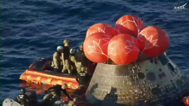 Rescue personnel standing on the front porch assist the Orion crew out of the module, both stationed in the Pacific Ocean