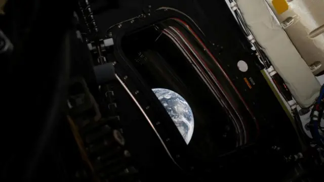 A semi circle of the Earth peaks out of a window on the Orion capsule.
