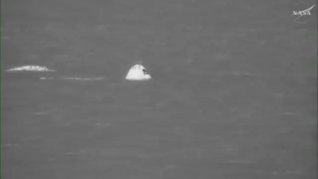 The Orion capsule seen in the Pacific Ocean, highlighted in bright white against the ocean's grey colour through a thermal camera effect