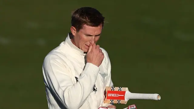 Zak Crawley going off the field with the bat tucked under his left shoulder