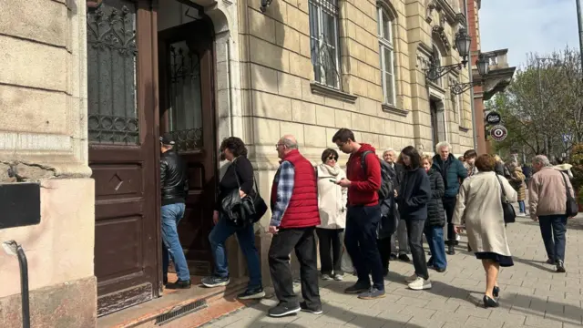 Hungarians line up to vote outside a Budapest polling station in the Újbuda district. A line is outside of the building along a street.