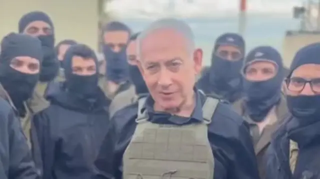 Benjamin Netanyahu wears an armour vest while surrounded by soldiers wearing black balaclavas.