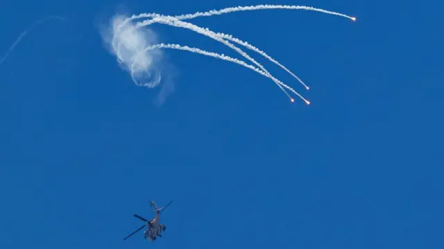 Disa fishekzjarre prodhojnë gjurmë të gjata tymi të bardhë pranë një helikopteri Apache izraelit.