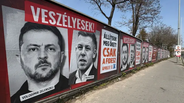 A wall of Hungarian election posters, showing Volodymyr Zelensky and Péter Magyar.in black and white