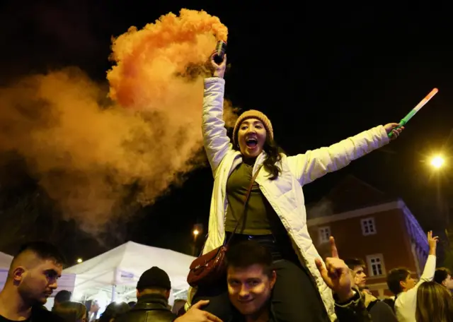 A woman lighting a flare while on someone's shoulders in Budapest