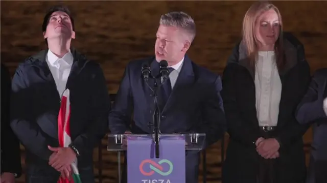 Magyar, who has greying hair in a short back and sides style and wears a suit and tie, speaks into mic on a lectern