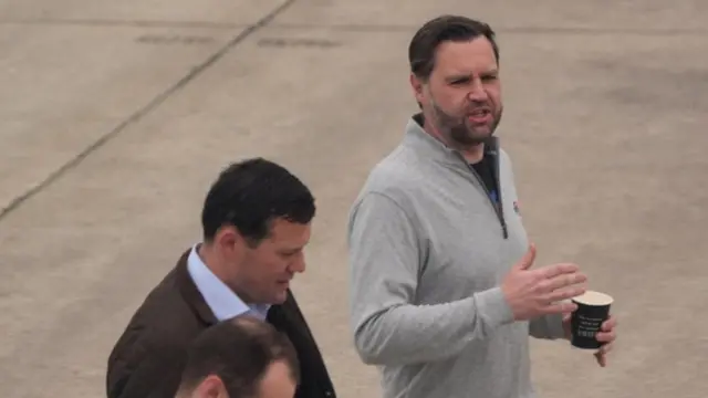 JD Vance in a grey zip up sweatshirt with a coffee