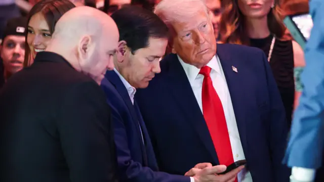 UFC CEO Dana White, Marco Rubio and Donald Trump huddle together in a crowded room, with Rubio showing both men something on his phone.