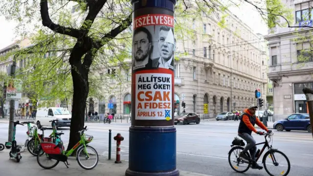 A cyclist going past an election poster depicting Volodymyr Zelensky next to Peter Magyar
