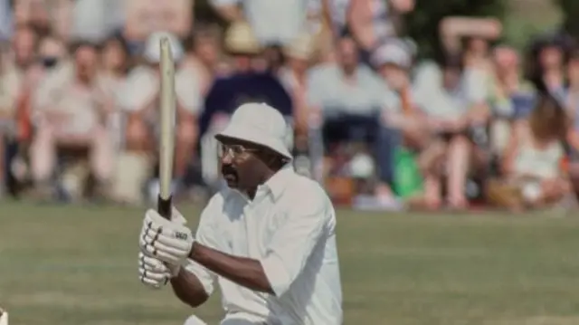 Clive Lloyd down on one knee, wearing a floppy hat and glasses, playing a pull shot