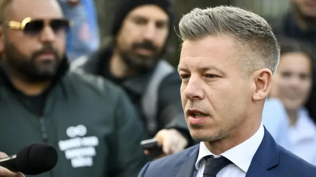Péter Magyar talks to media while wearing a navy suit and a black tie.