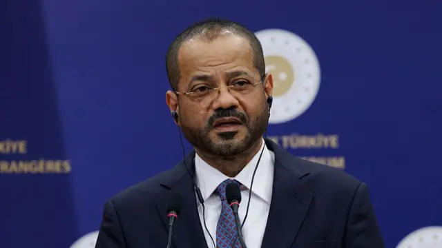 Omani Foreign Minister Badr Albusaidi wears a dark suit and tie while speaking against a purple background.