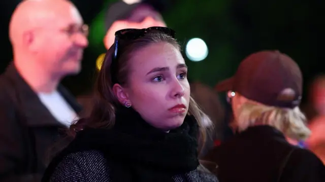 A woman pouts her lip in a crowd of people following the partial results of the Hungarian parliamentary election