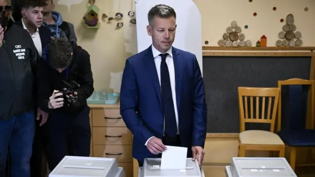 Péter Magyar places his vote in a ballot box during the general election in Budapest, Hungary, 12 April 2026. He is wearing a navy suit and a dark coloured tie.