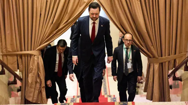 Vice-President JD Vance walks up a flight of stairs with his head looking down to the floor and several men walking up behind him.
