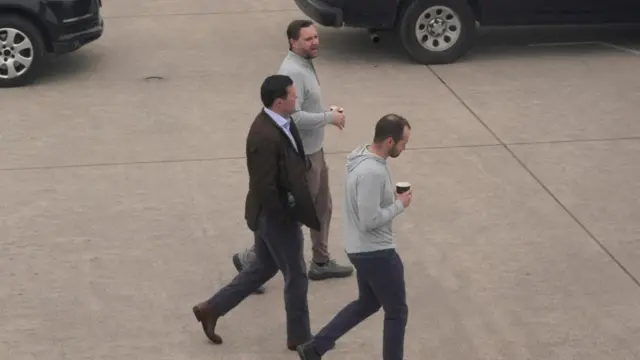 JD Vance in a grey zip up sweatshirt with a coffee and two aides