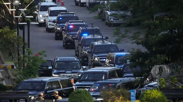 A line of black cars on a road in Pakistan, some have flashing blue lights.