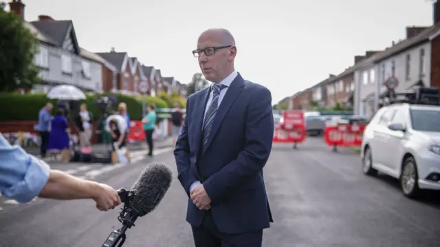A man in a suit speaks to reporters in a street in Southport