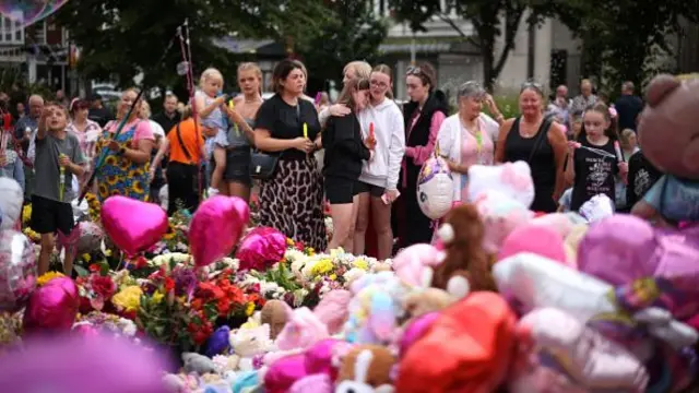 Women cry at a vigil surrounded by flowers