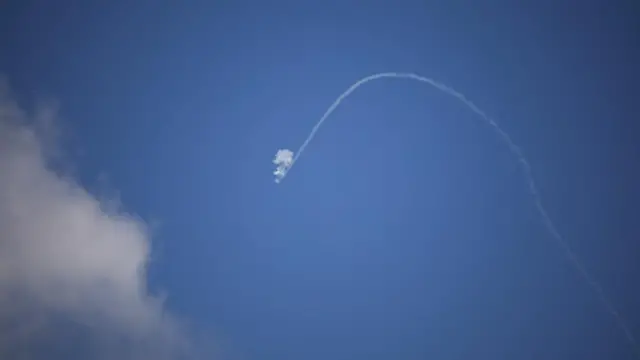 Israeli anti-missile system operates for an interception, over the Israel-Lebanon border, with a trail ending suddenly in a plume of smoke in the blue sky. A cloud is visible on the left