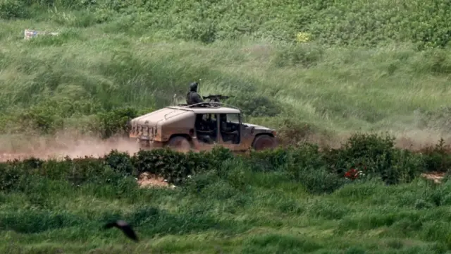 An Israeli military vehicle kicking up dust, with a soldier manning a machine gun on the roof