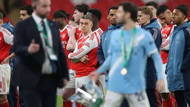 Arsenal players looks at a Manchester City player holding the Carabao Cup