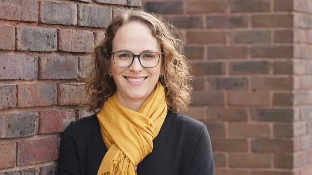 A woman wearing a yellow scarf, looking directly at the camera.