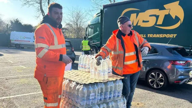 Two men stood giving out water bottles.