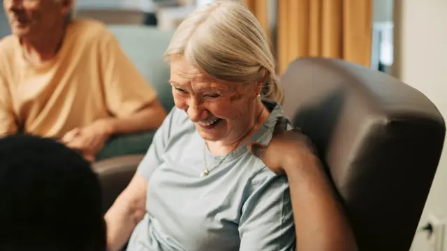 A caregiver puts his hand on the shoulder of an older person who is seated
