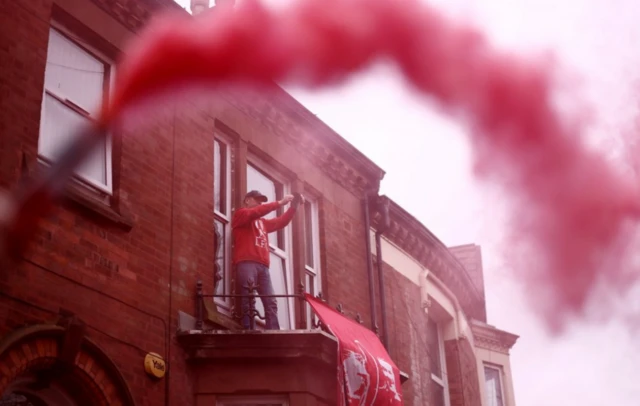 Liverpool fan stands on the balcony of a house with a large banner seen outside the stadium