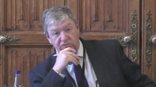 A man with short, white hair wearing a dark suit.