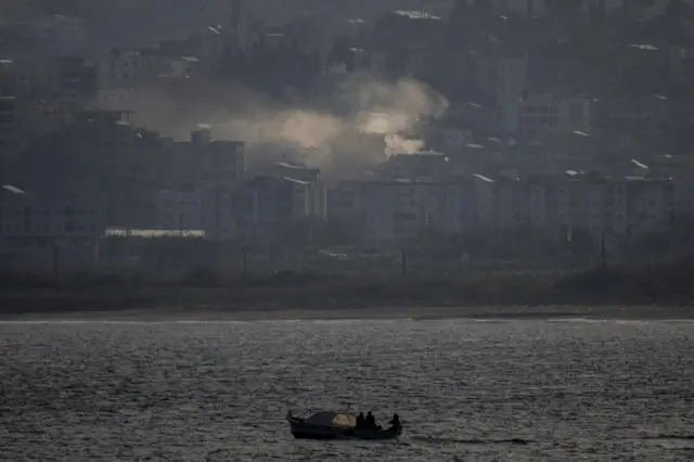 Fishermen sail their boat as smoke from an airstrike rises in Tyre